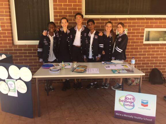six students standing behnd sign and table