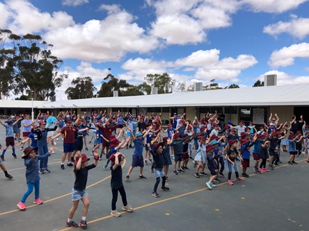 Dozens of students are assembled in a courtyard dancing.