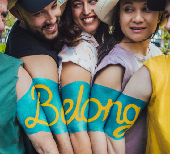 group of people with the word Belong painted across their arns which are joined together from shoulder to elbow