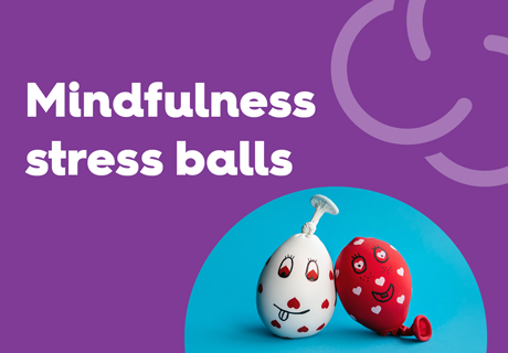 A purple background with the text 'Mindfulness stress balls' in bold white letters. Below, a circular cutout reveals two stress balls made from balloons filled with material, each decorated with smiling faces. One is white with red heart designs, and the other is red with white heart patterns. The background of the cutout is blue.