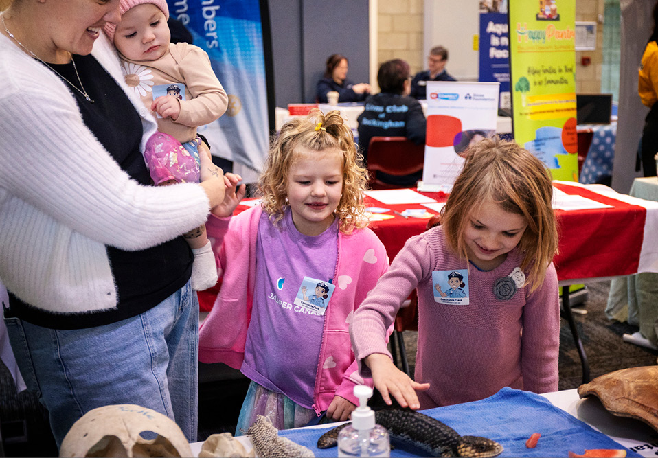 A mother carrying a baby with two young children looking at reptiles on a table.