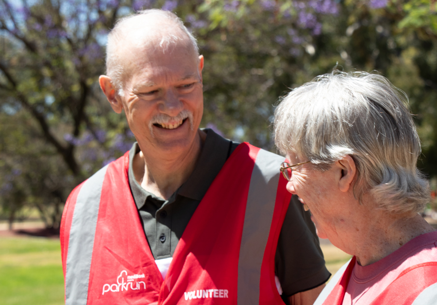 Two people in red volunteer vests smiling at each other.